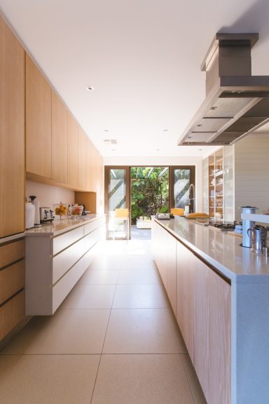 Helle moderne Küche mit Holzschränken und großen Fenstern, die auf einen Garten blicken.